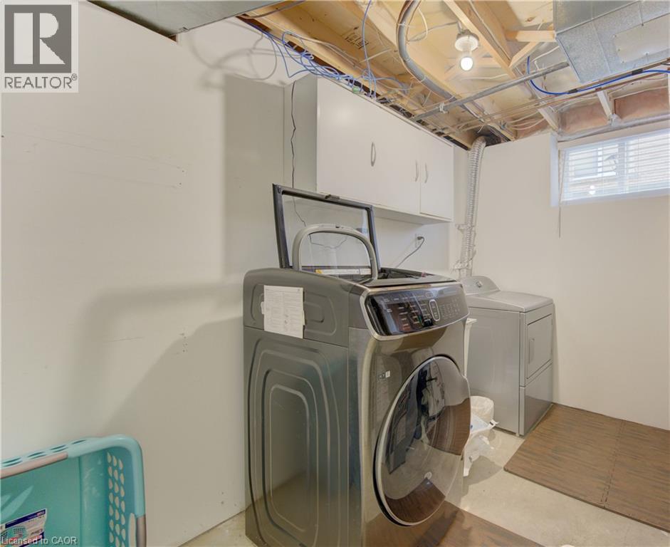 Dedicated laundry area featuring a light gray washer and dryer set, white wall-mounted cabinetry, and a single window with blinds