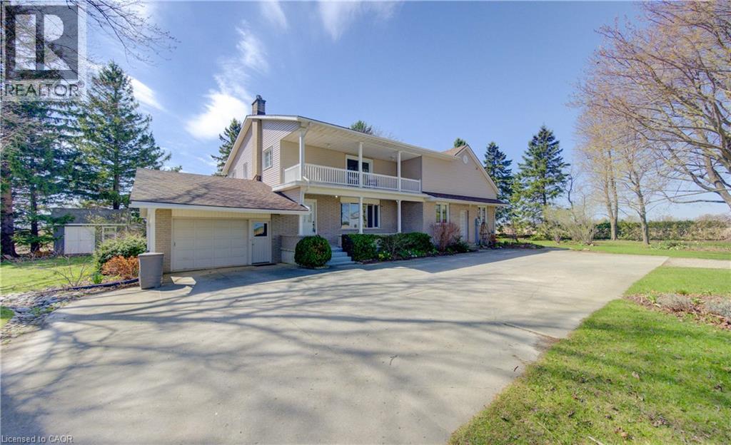 Spacious paved driveway leading to a two-story residence with an attached garage, upper-level balcony, and mature surrounding landscaping