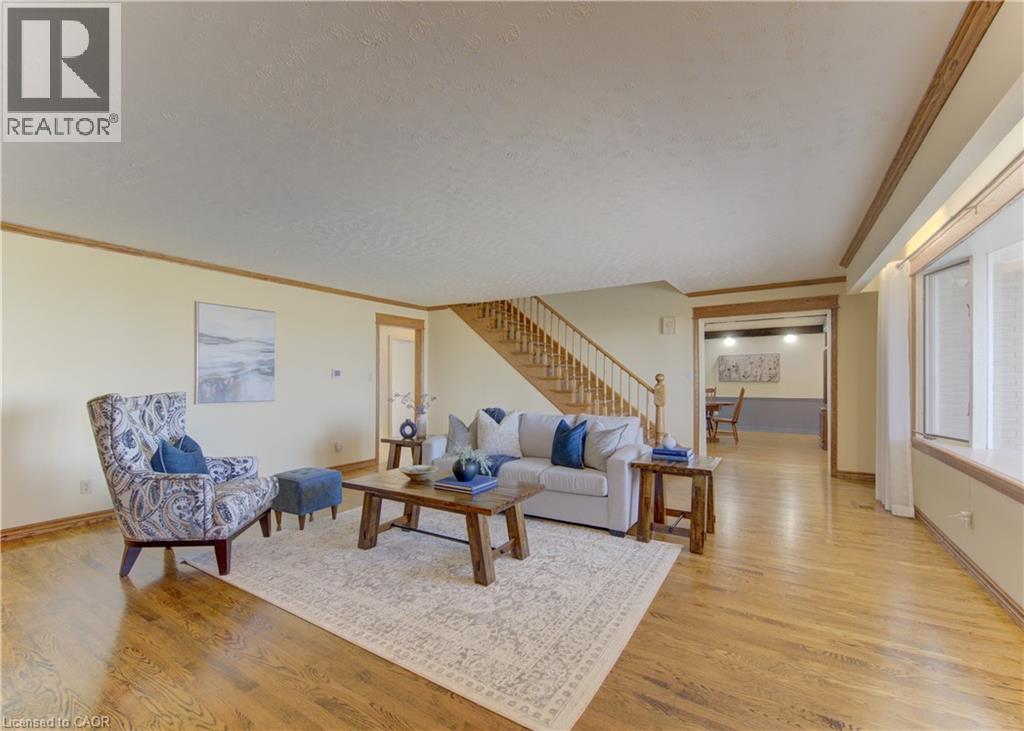 Spacious living area featuring polished wood flooring, a prominent staircase with wood balusters, and a large bay window