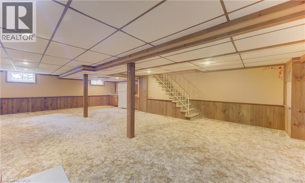 Spacious finished basement featuring wood-panel wainscoting, drop ceiling with recessed lighting, and a straight staircase with metal railings