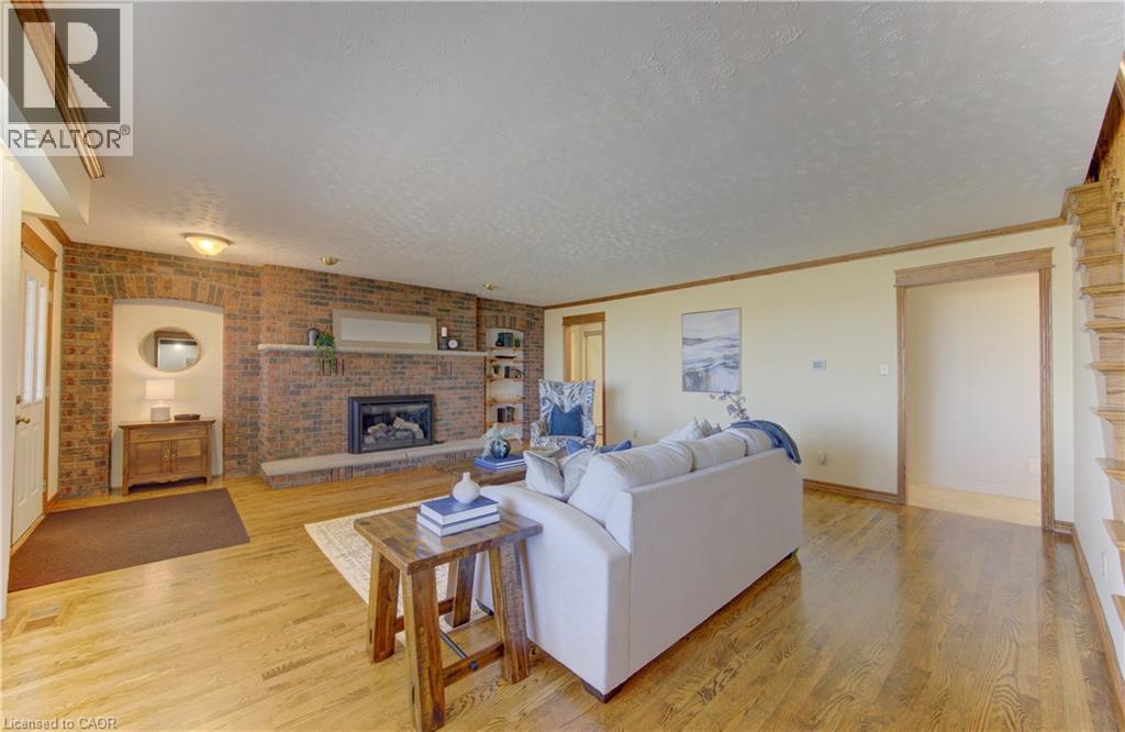 Spacious living area featuring light wood-finish flooring, a prominent brick fireplace with a stone mantel and hearth, and exposed brick walls