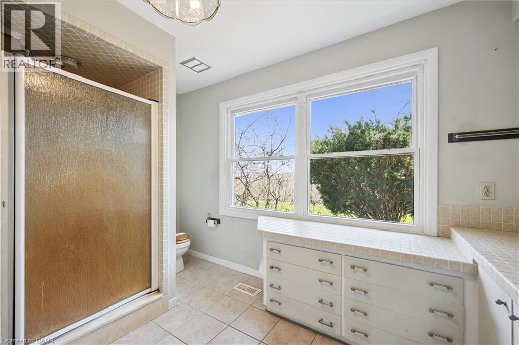 Bathroom featuring a tiled shower enclosure, a large window, custom-built cabinetry with multiple drawers, and tiled flooring