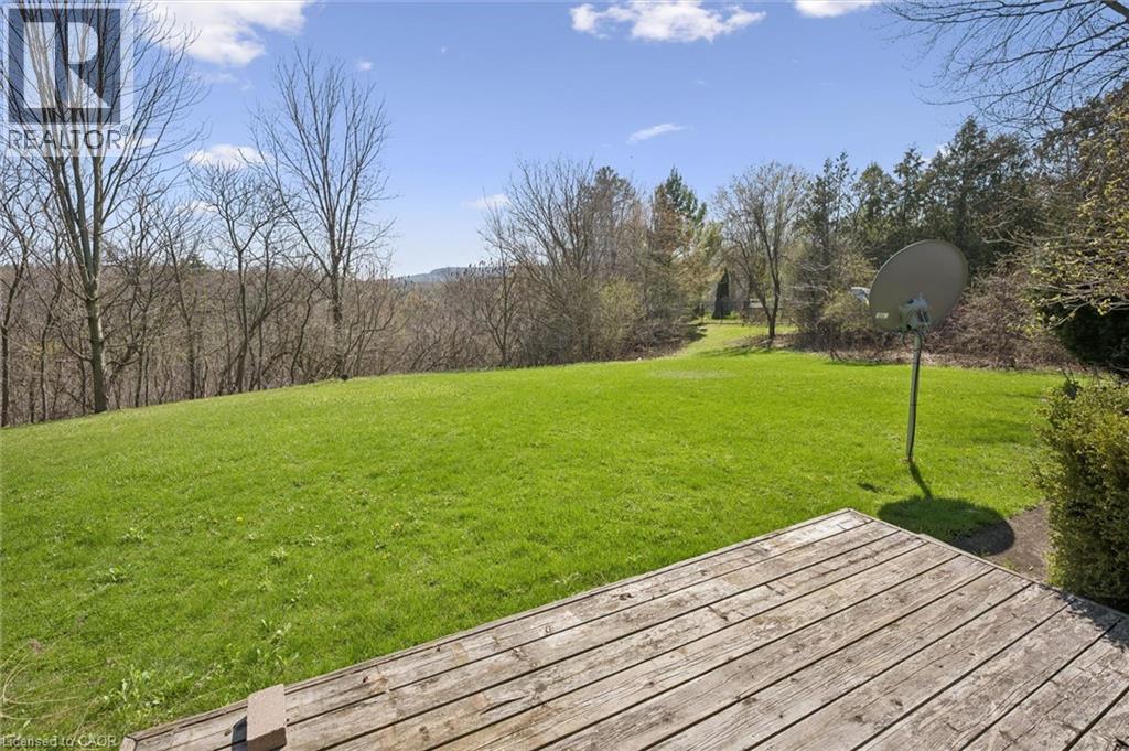 Expansive outdoor space featuring a wood deck, a large grassy area, and mature trees bordering the property