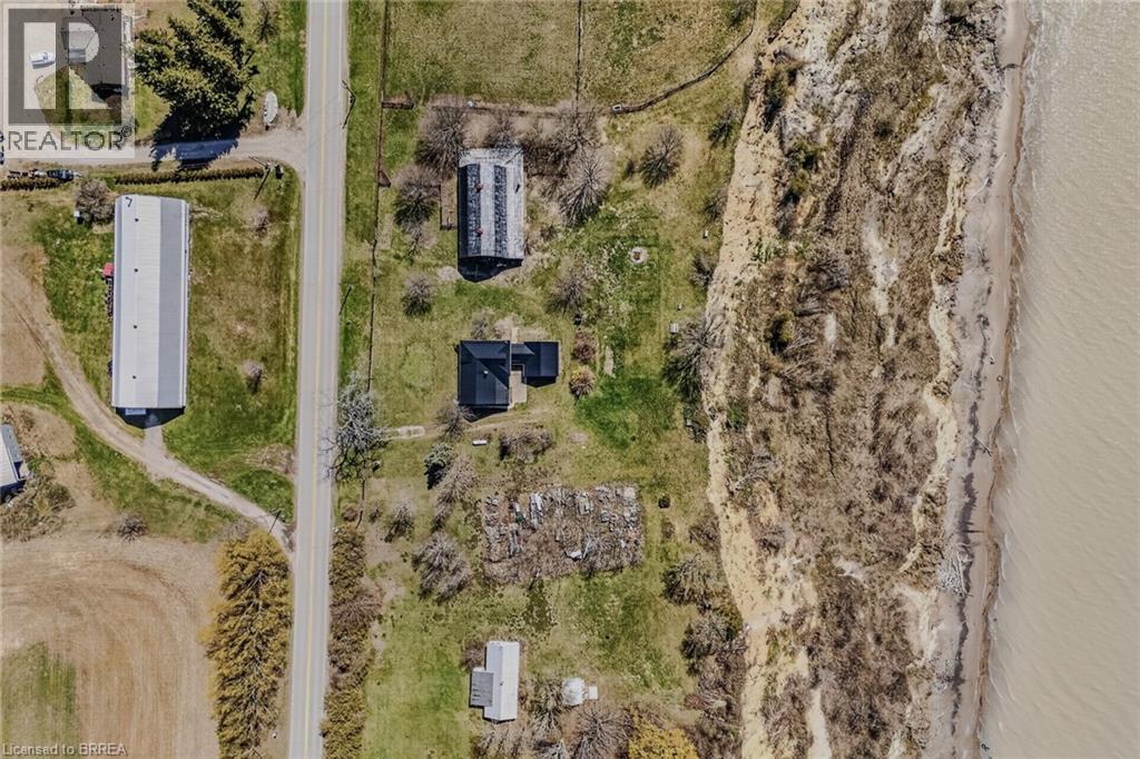 Expansive aerial showcasing a significant property footprint, including a long building with a light-toned roof, a smaller structure with a dark roof, and direct adjacency to a natural cliffside leadi