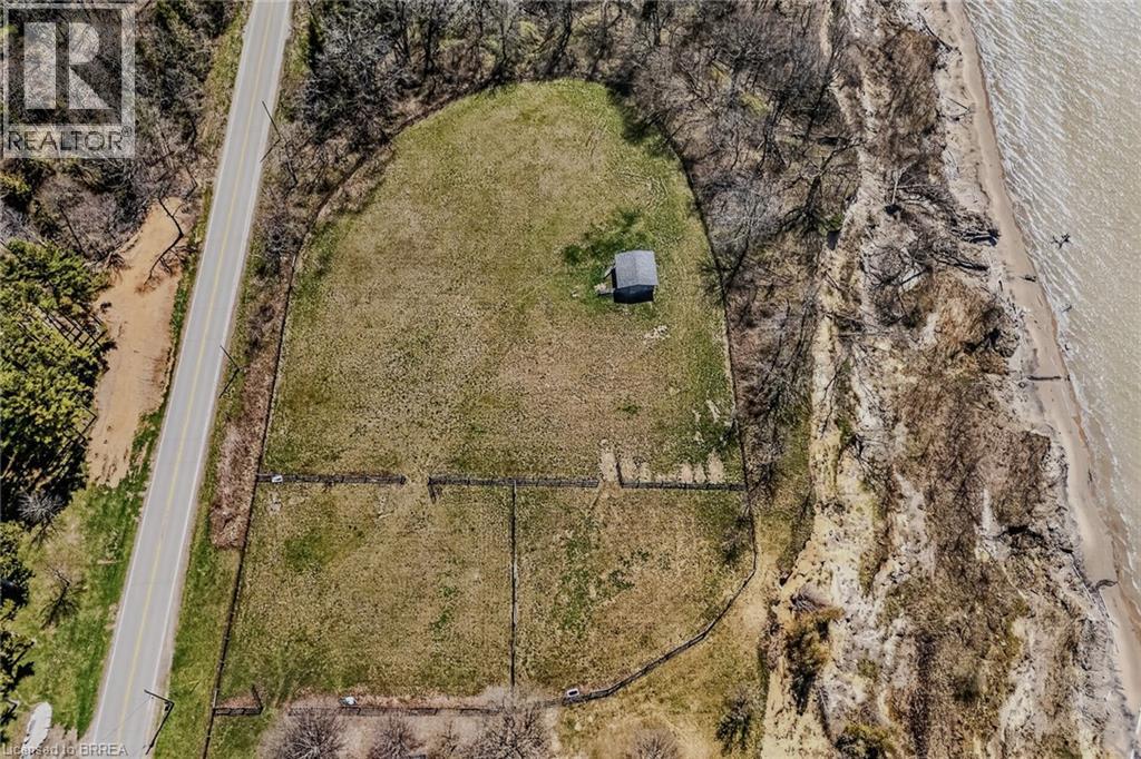 Expansive land parcel featuring a small structure, bordered by a paved road, natural tree lines, and a sandy waterfront