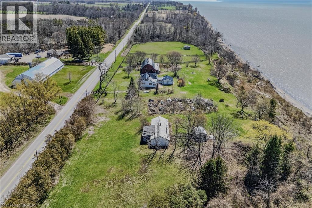 Expansive waterfront property featuring multiple structures, verdant green spaces, mature trees, a paved road traversing the property, and a substantial body of water