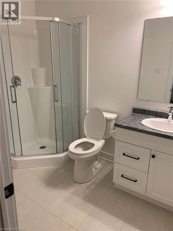 Bright bathroom featuring a corner shower enclosure with clear glass, a white vanity with shaker-style doors and drawers, a dark countertop, an integrated sink, and light-toned tile flooring