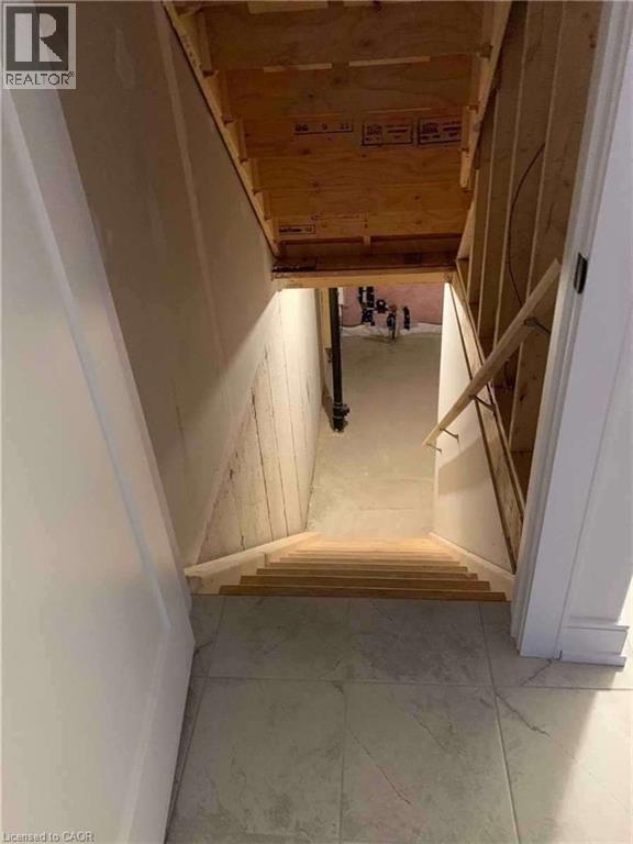 Unfinished basement access featuring wood stairs and rough-in framing, with concrete walls and flooring