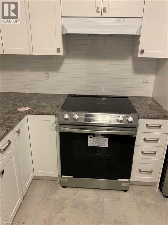 Contemporary kitchen featuring a stainless steel range, crisp white cabinetry, light-toned countertops, a subway tile backsplash, and tile flooring