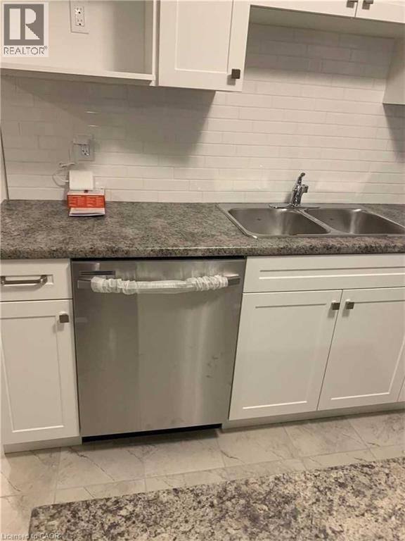 Kitchen featuring a stainless steel dishwasher, dual basin sink with chrome faucet, light-toned countertop, white subway tile backsplash, and white shaker-style cabinetry with dark square pulls