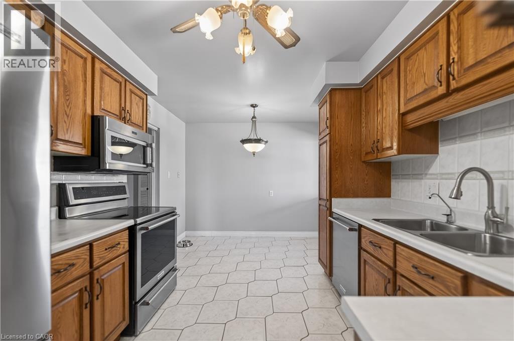 Kitchen featuring stainless steel appliances, wood finish cabinetry, light countertops, and hanging light fixtures