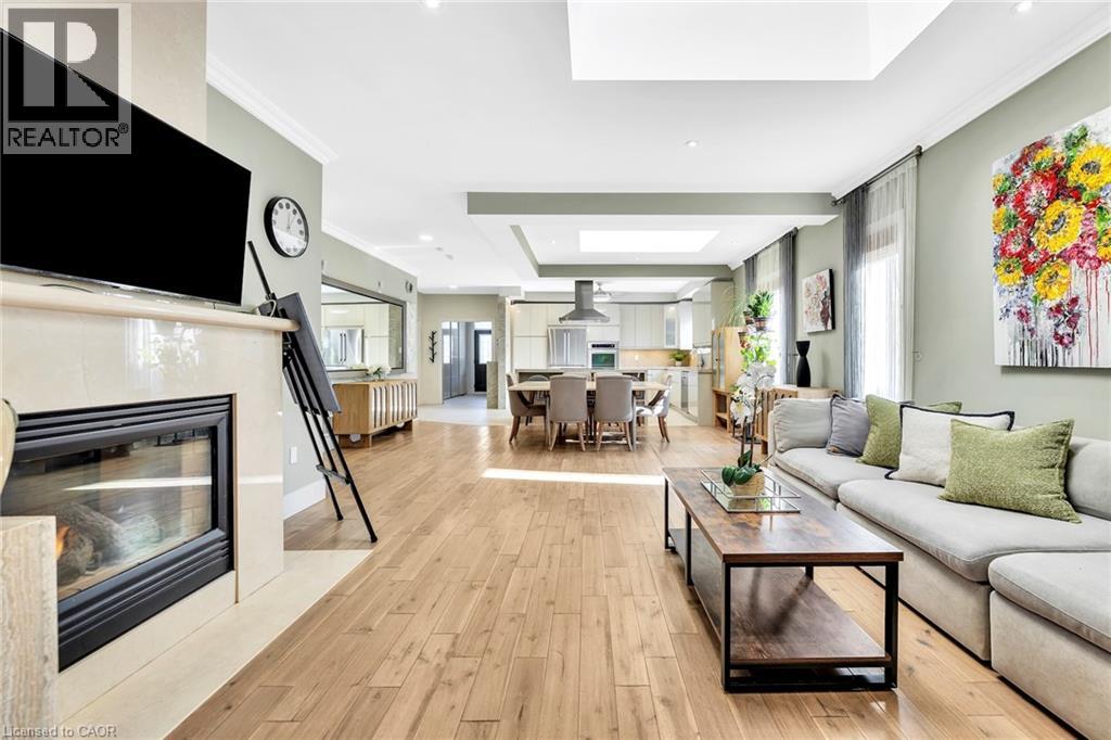 Open-concept living area featuring wood-finish flooring, a tiled fireplace, crown molding, and recessed lighting