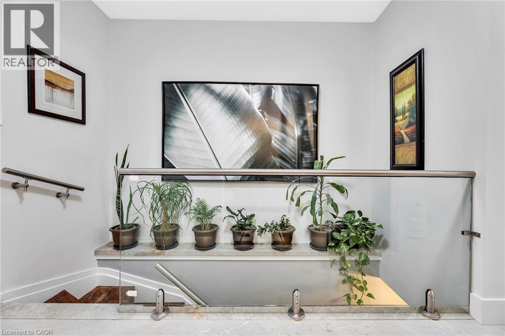 Modern staircase featuring a glass and stainless steel railing, a matching stainless steel wall-mounted handrail, and a marble landing