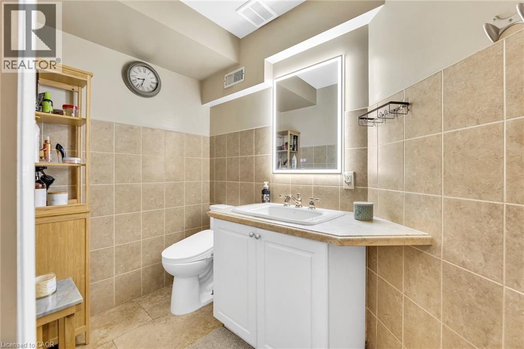 Bathroom featuring full-height tiled walls, an illuminated vanity mirror, a corner vanity with an integrated sink, white cabinetry, and recessed lighting