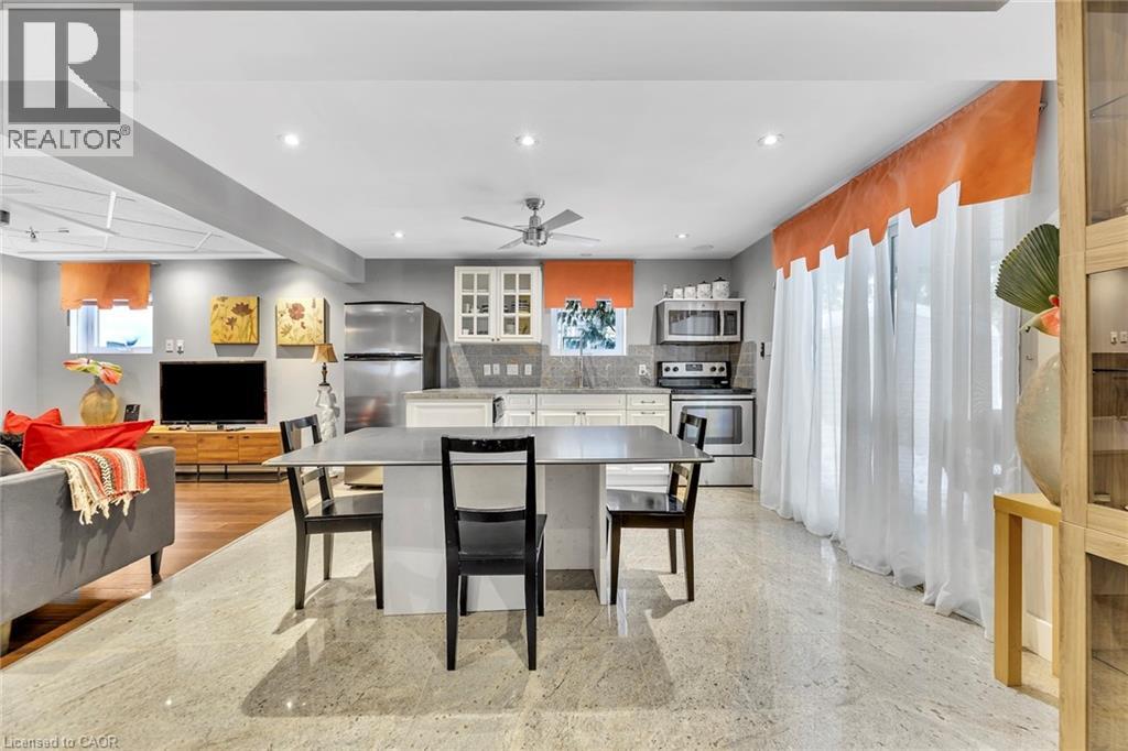 Open-concept living space featuring expansive light-toned flooring, a modern kitchen with stainless steel appliances, white cabinetry, and a ceiling fan