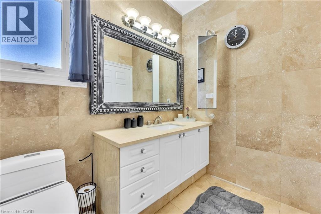 Bathroom featuring floor-to-ceiling natural stone tile, a white vanity with drawers and cabinet storage, a light-toned countertop, and a large decorative mirror with an overhead light fixture