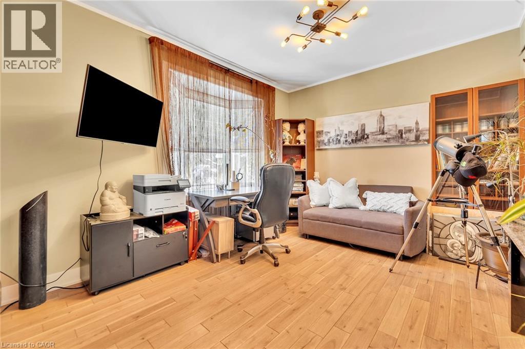 Room featuring wood-finish flooring, a contemporary multi-bulb ceiling fixture, a window with sheer curtains, warm-toned wall paint, and built-in shelving