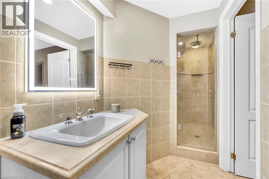 Bathroom featuring a built-in vanity with a drop-in sink, an illuminated mirror, a glass-enclosed shower, and a tiled floor