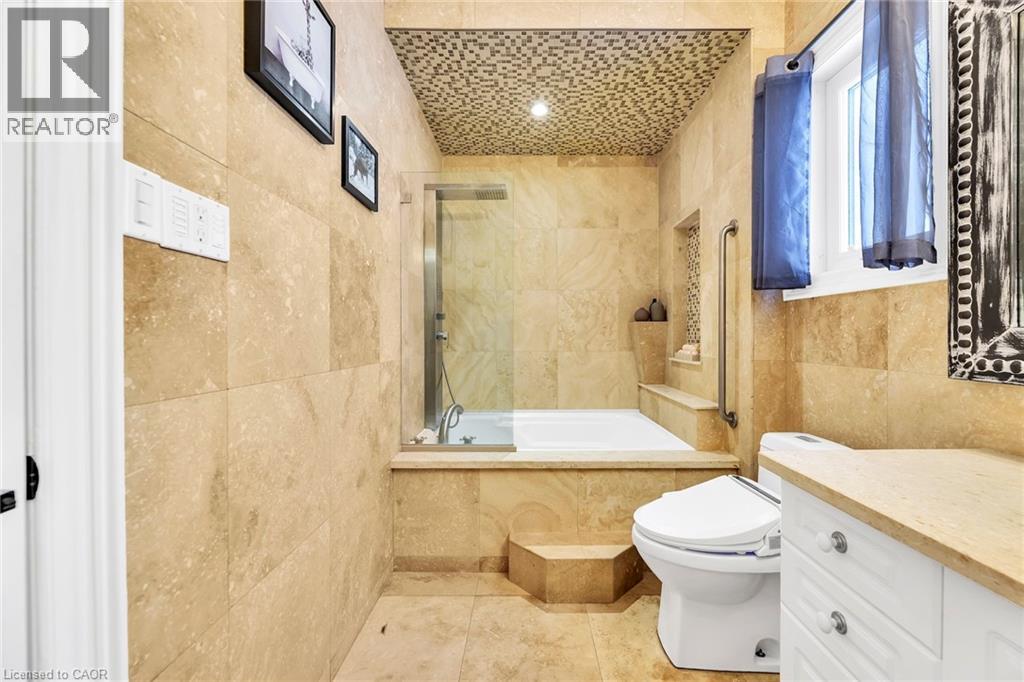 Bathroom featuring extensive stone-look tilework, a built-in tub with a glass enclosure, an integrated niche, a window, and a built-in vanity with a countertop