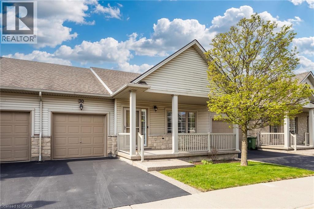 Exterior featuring vinyl siding, stone accents, asphalt shingle roofing, a covered porch with white railings, and a two-car garage with panel doors