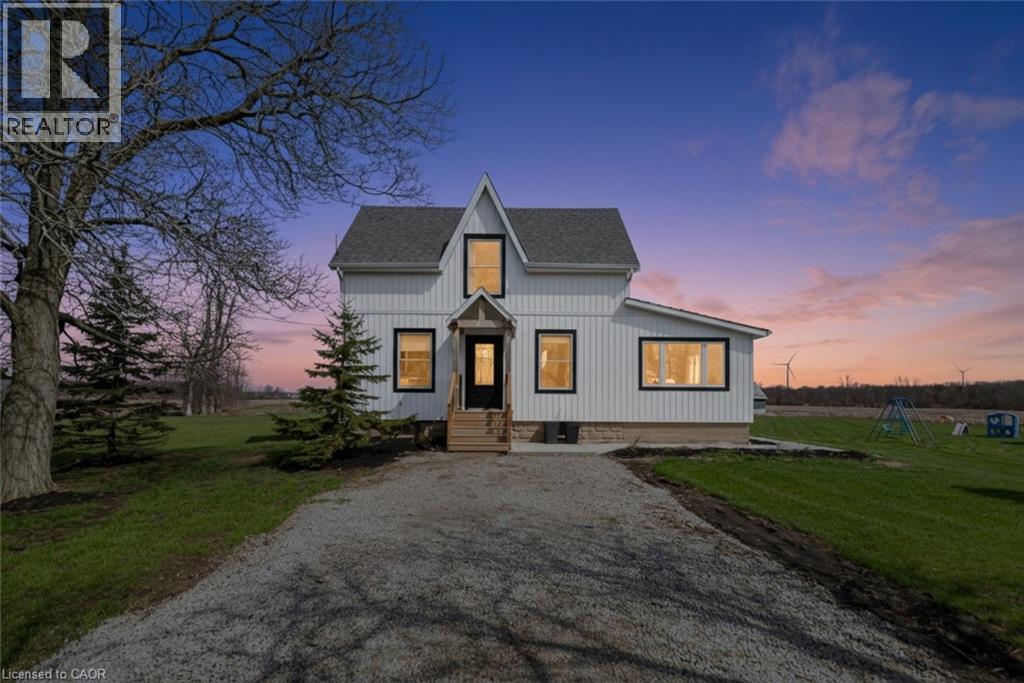 Modern farmhouse exterior featuring white vertical siding, black-framed windows, a dark shingled roof, a prominent front gable, and a gravel driveway