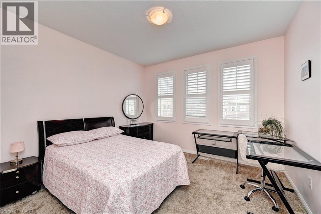 Bedroom featuring plush carpeting, three windows with plantation shutters, and a ceiling-mounted light fixture