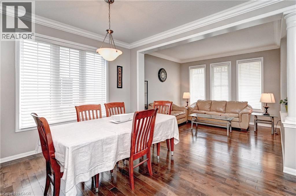 Open-concept living and dining areas featuring dark wood-finish flooring, extensive crown molding, and large windows with blinds