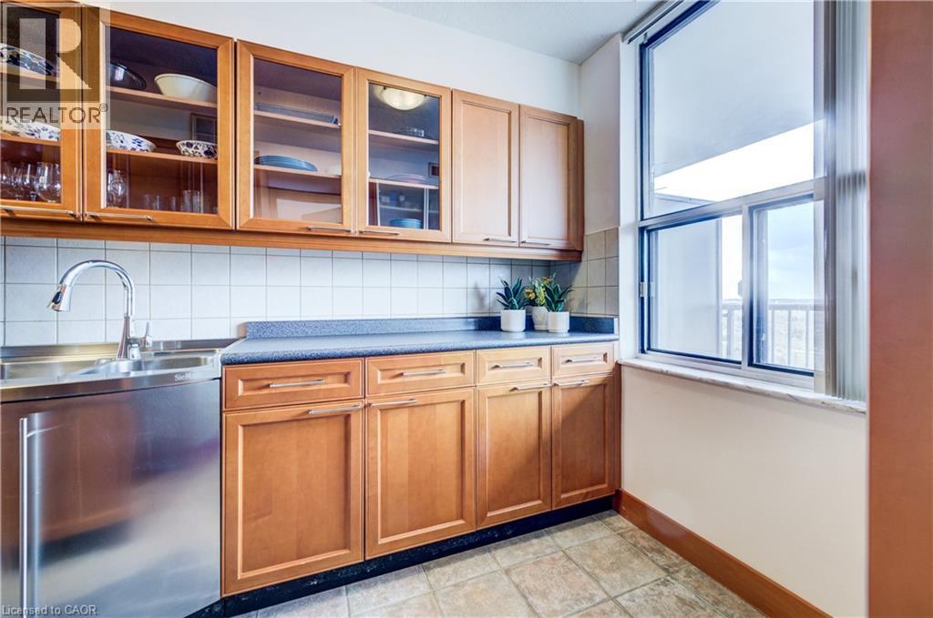Kitchen featuring tasteful backsplash, glass fronted cabinets, wood finish cabinetry, dark countertops, and stainless steel dishwasher