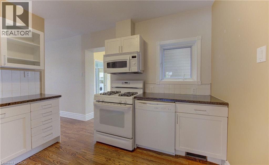 Kitchen featuring white cabinetry, dark speckled countertops, a white tile backsplash, and wood-finish flooring