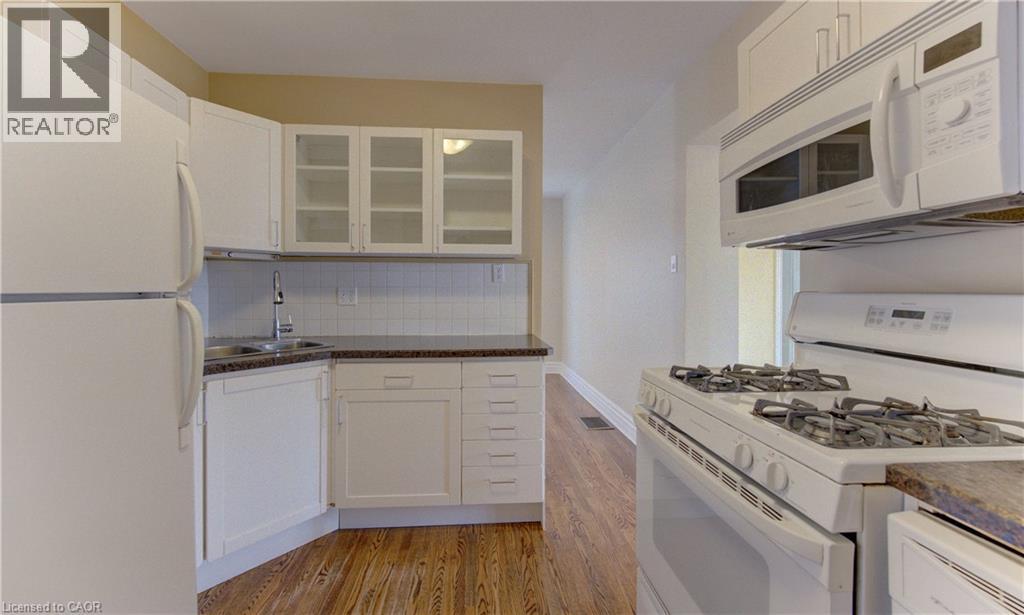 Kitchen featuring white cabinetry, white appliances, dark countertops, a tiled backsplash, and wood-finish flooring