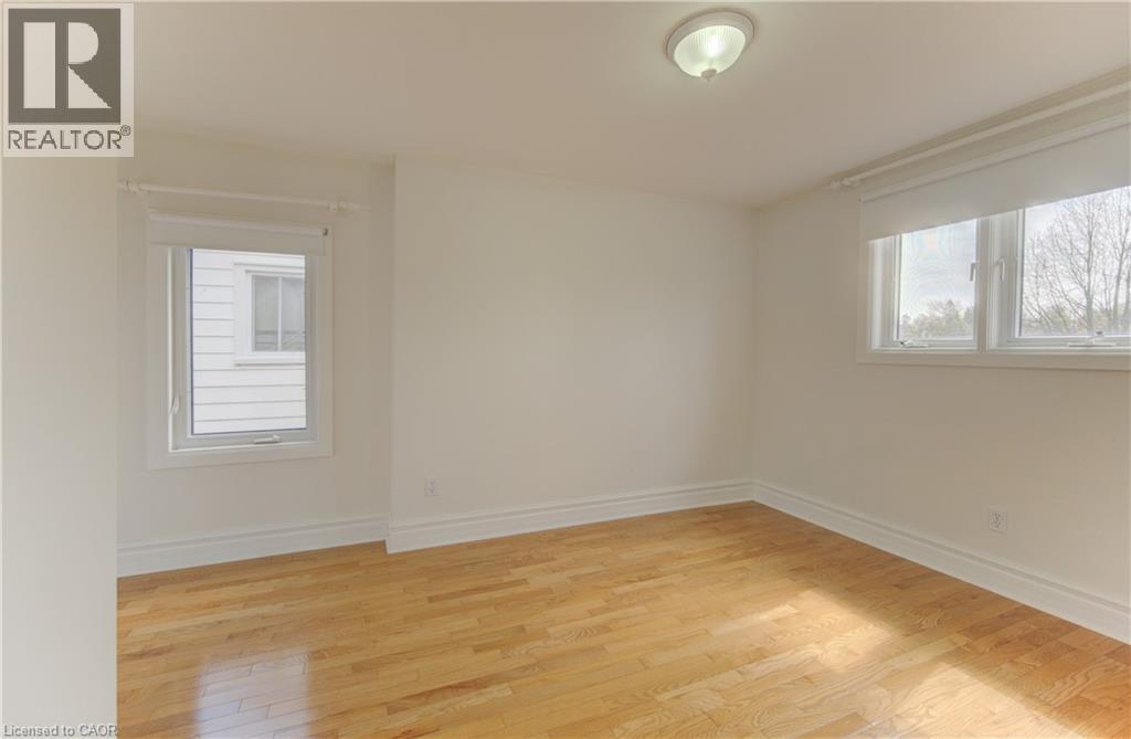 Room featuring two windows, wood-finish flooring, white baseboards, and a flush-mount ceiling light fixture