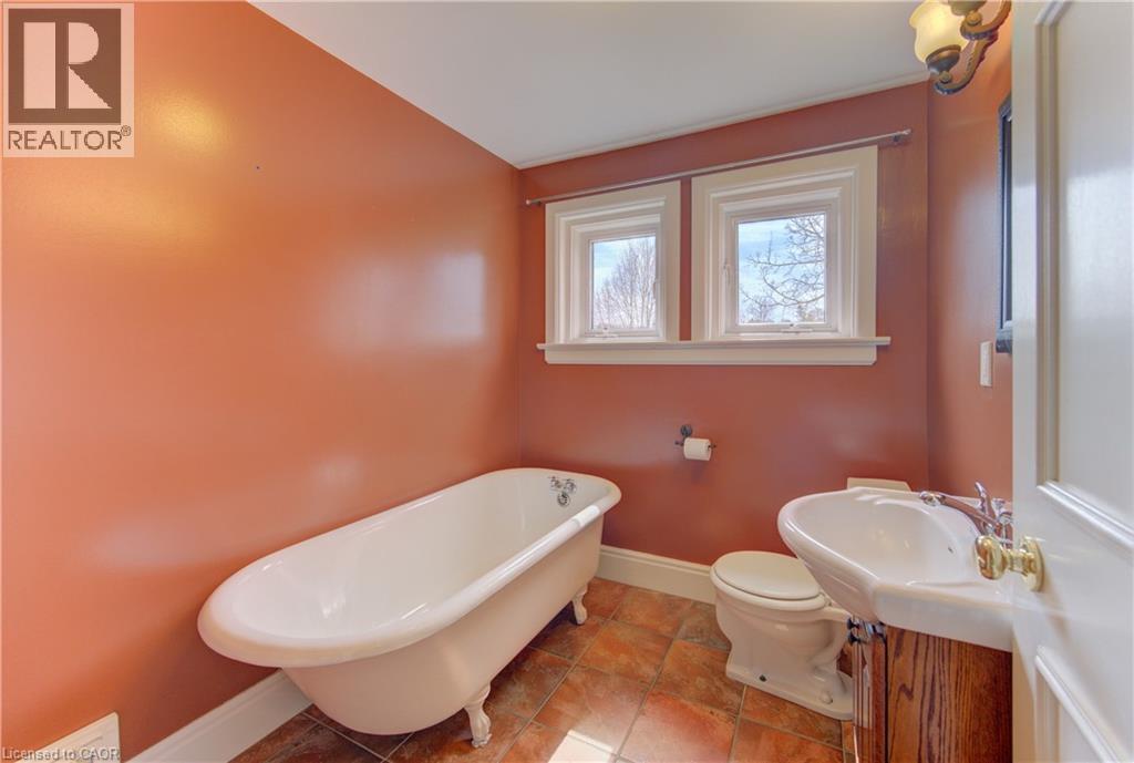 Bathroom featuring a classic clawfoot bathtub, pedestal sink with brass-finish fixtures, and a dual window configuration
