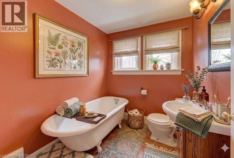 Freestanding clawfoot tub with a wood-finish tray, dual windows with natural light, a wood-finish vanity with an integrated sink, and an overhead vanity light fixture