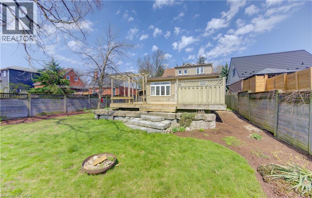 Expansive backyard featuring a manicured lawn, a wooden deck with a privacy screen and pergola, and a stacked stone retaining wall