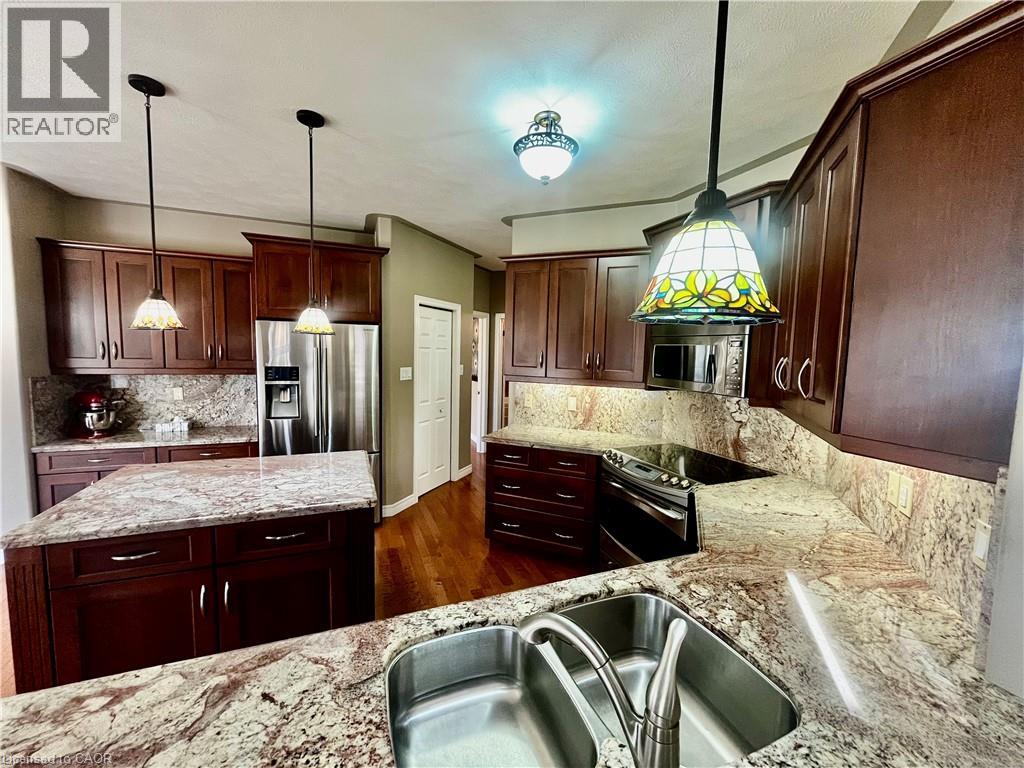 Spacious kitchen featuring rich wood cabinetry, stainless steel appliances, a center island, extensive stone countertops with matching backsplash, and a double basin sink