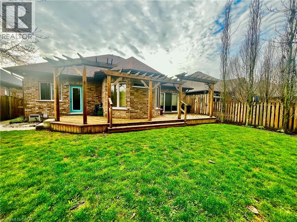 This property features a brick exterior, a spacious wooden deck with a pergola, and a vibrant green lawn