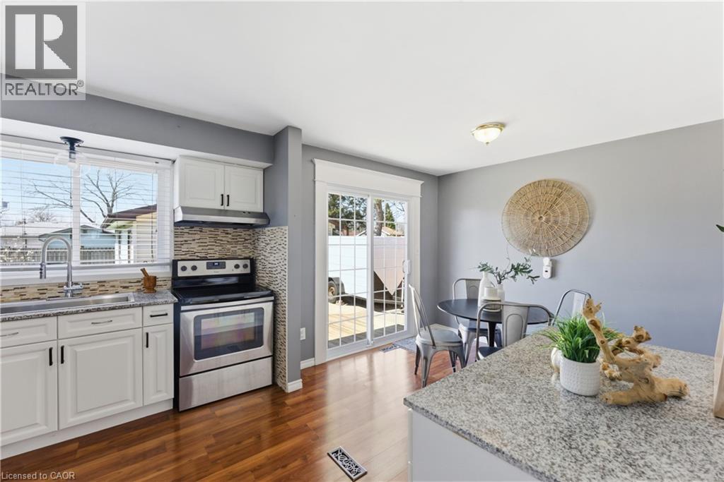 Kitchen and dining area featuring wood-finish flooring, white cabinetry, granite countertops, and a tile backsplash