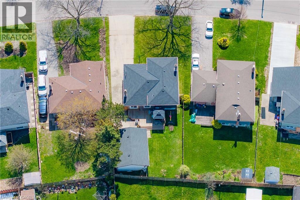 Aerial perspective showcasing property with a dark shingle roof, expansive green lawn, and a rear deck