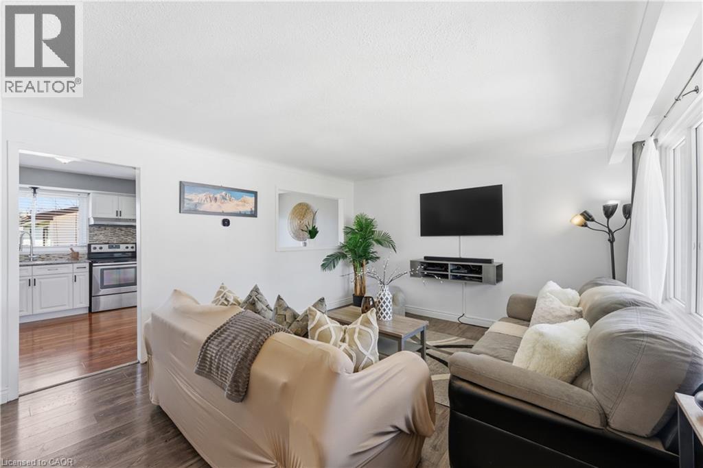 Living area featuring wide plank wood-finish flooring, white wall paint, and a large window with sheer drapes