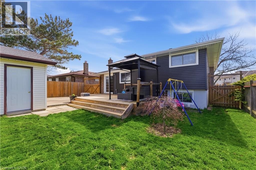 Rear exterior featuring a wooden deck with gazebo, dark siding, multiple windows, a detached shed, and a fenced perimeter