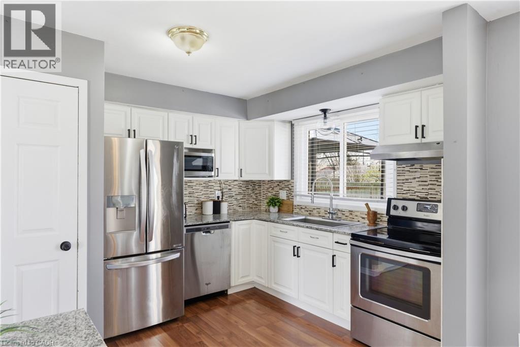 Modern kitchen featuring white cabinetry, stainless steel appliances, wood-finish flooring, granite-style countertops, and a mosaic tile backsplash
