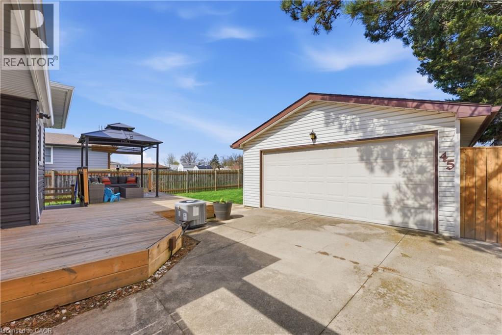 Detached garage with white siding and a brown roof, featuring a concrete driveway, an expansive wooden deck, and a fenced perimeter