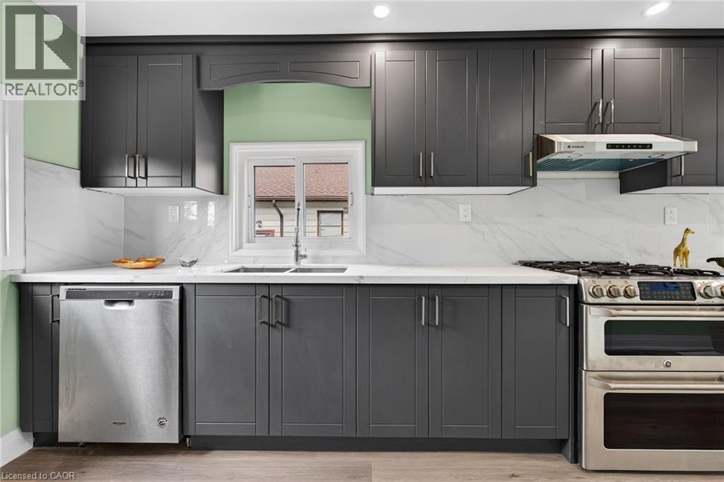 Contemporary kitchen featuring dark shaker-style cabinetry, light countertops, a stainless steel gas range with a matching range hood, a stainless steel dishwasher, and a double basin sink