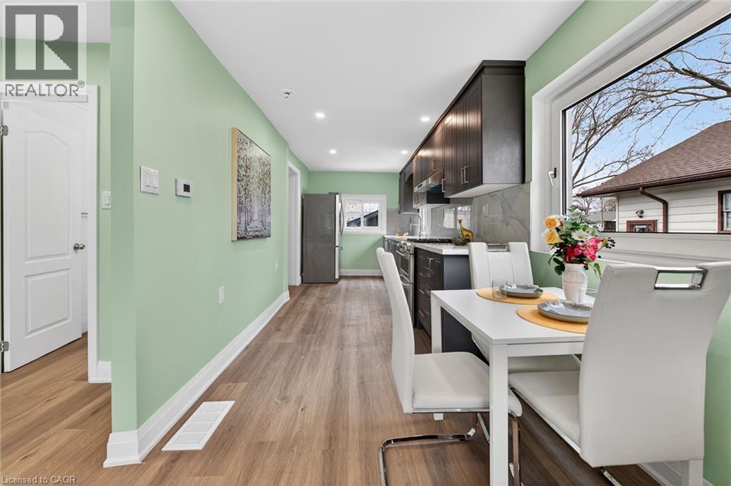 Contemporary kitchen and dining area featuring wood-finish flooring, recessed lighting, dark cabinetry, light countertops, and a stone-finish backsplash