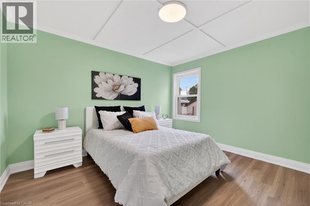 Bedroom featuring light green walls, wood-finish flooring, a single window, white trim, and a ceiling light fixture
