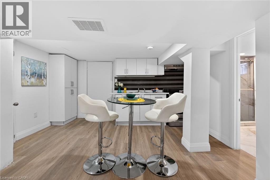 Compact kitchen area featuring white cabinetry, a black and white striped tile backsplash, stainless steel appliances, and wood-finish flooring