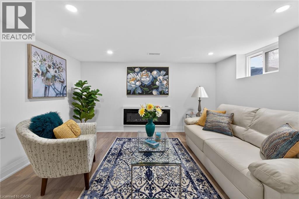 Recessed lighting illuminates a room featuring light wood-finish flooring, a wall-mounted electric fireplace, and a high-set window