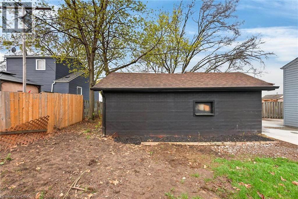 Detached garage featuring dark horizontal siding, a brown shingled roof, and a small window