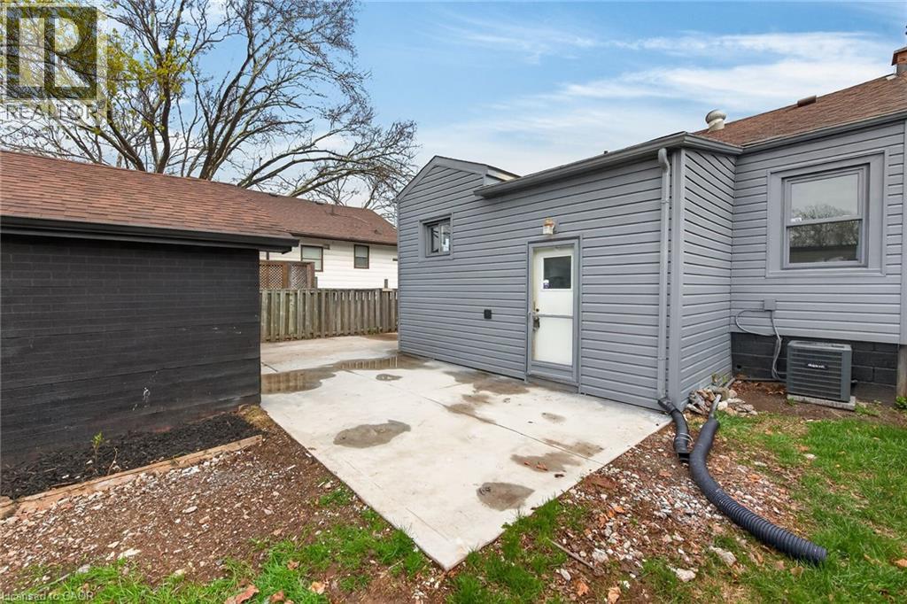 Rear exterior featuring gray horizontal siding, a white service door, and a concrete patio