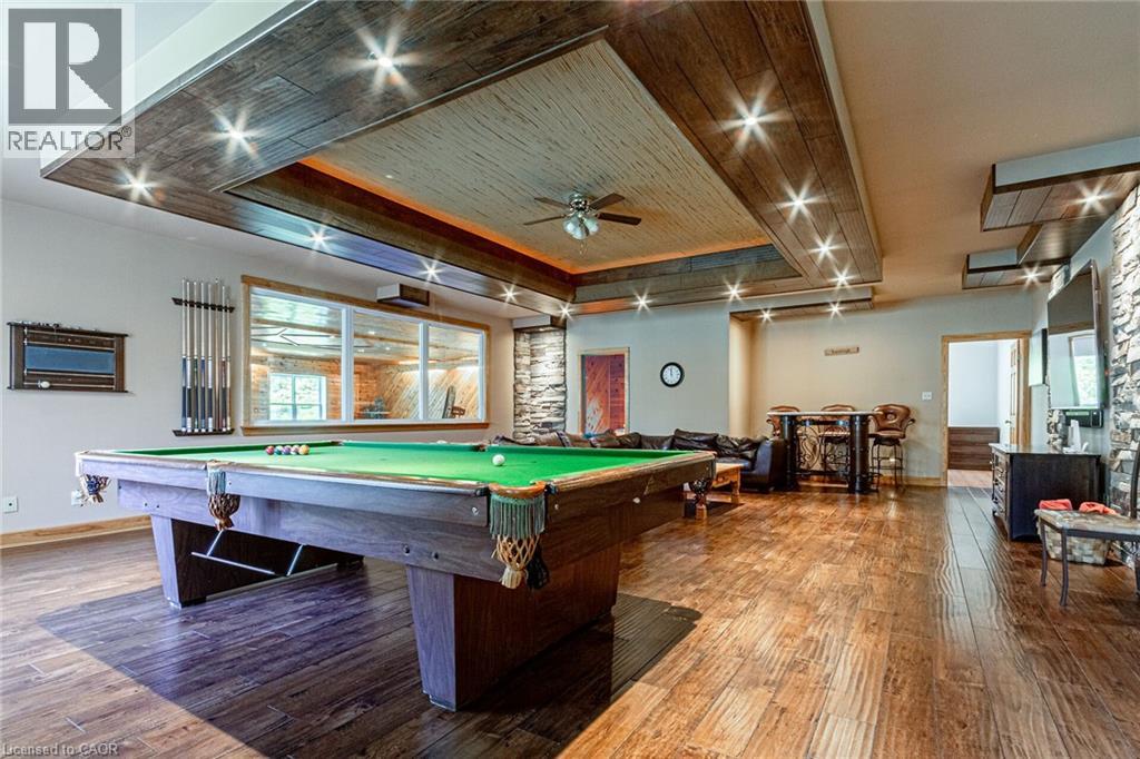 Spacious entertainment area featuring wood-finish flooring, a full-sized billiards table, recessed lighting, stone accent walls, and a built-in bar
